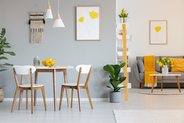 Two white lamps above a round dining table in open space apartment interior with yellow blanket on...