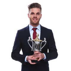 portrait of young businessman in navy suit holding a trophy