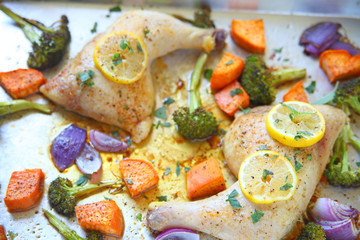 Overhead of chicken quarters with broccoli, sweet potatoes, onion and lemon