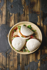 Asian sandwich steamed gua bao buns with pork belly, greens and vegetables served in ceramic plate...