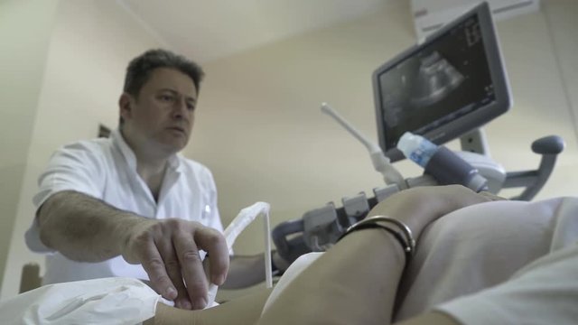 Gynecologist performing medical review of woman with ultrasound, doctor looking in monitor on gynecological examination, female patient lying on bed in ambulance room at gynecology ward, health care
