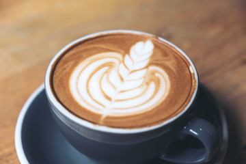 Closeup image of a blue cup of hot latte coffee with latte art on vintage wooden table in cafe