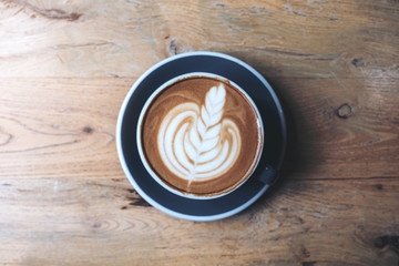 Top view image of a blue cup of hot latte coffee with latte art on vintage wooden table in cafe