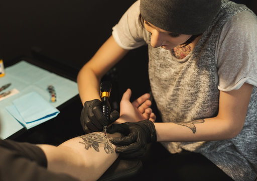 Young woman tattooist doing tattoo on male arm