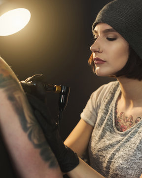Young woman tattooist doing tattoo on shoulder