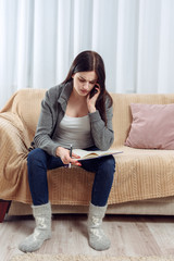 Obraz premium woman writing on a notebook on a couch and consulting on the phone in a living room