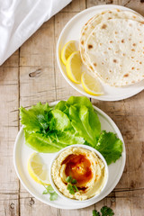 Hummus with olive oil and paprika, served with pita, lemon and lettuce leaves.