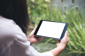 Mockup image of woman's hands holding black tablet pc with blank white desktop screen and green...