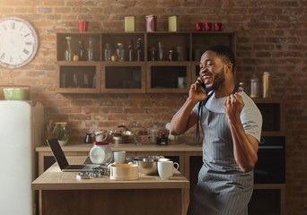 Happy african american man talking on smartphone in kitchen