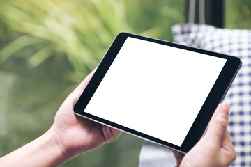 Mockup image of hands holding black tablet pc with white blank desktop screen with green nature background