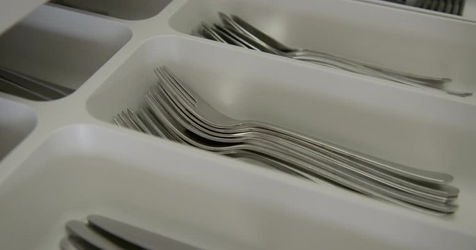Pan on close-up woman's hand as she opens drawer full of stainless steel cutlery, focus on forks. Draw closed again in kitchen. Real time side angle 4K