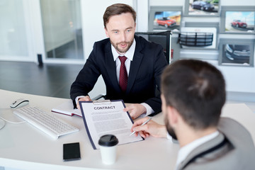 Fototapeta na wymiar Portrait of handsome businessman showing contract for signing to partner sitting across desk in modern office, copy space