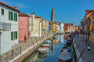 Fototapeta na wymiar Colorful buildings, tower, people and boats in front of a canal at Burano, a gracious little town full of canals, near Venice. In the Veneto region, northern Italy