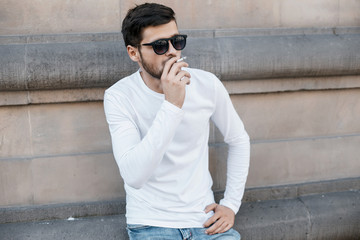 Obraz premium A young man travels through the streets of the city. Boy in sunglasses Stylish man near the building. The man sits on a whip. Beard and hair in a stylish guy.
