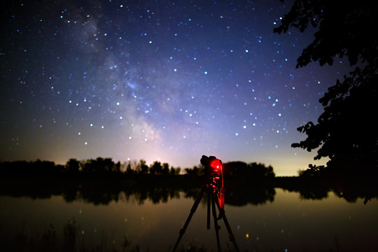 The camera on the tripod takes pictures of stars of open space in the night sky.