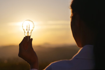 Portrait of a woman (girl) holding a light bulb with the sunset in the backgroud. Concept: Energy,...
