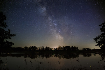 Space with stars in the night sky. The landscape with the river and trees is photographed on a long exposure.