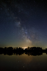 Fototapeta premium Space with stars in the night sky. The landscape with the river and trees is photographed on a long exposure.