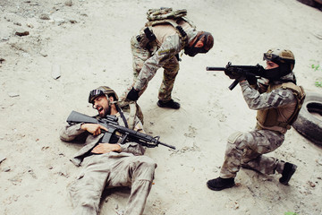 Fototapeta premium Dramatic picture of guy got wounded. His comrade is trying to pull him out of the battlefield. The third guy is defensing them.