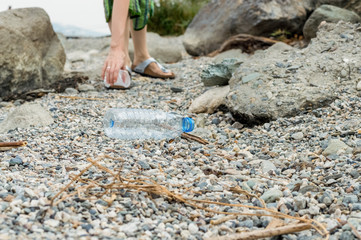 Young woman picking up the plastic bottle garbage, cleaning on the coastal strip.