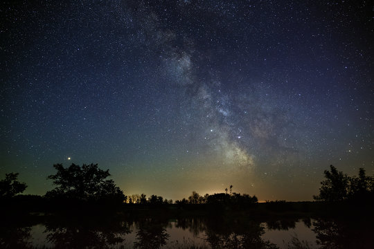 Space with stars in the night sky. The landscape with the river and trees is photographed on a long exposure.