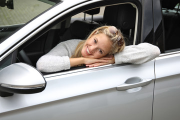 Hübsche blonde Frau lehnt lachend aus dem Fenster ihres Autos