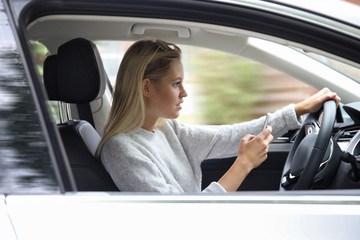 Hübsche blonde Frau hält während des Autofahrens ein Smartphone in den Händen