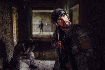 A picture of soldiers standing in dark corridor of empty building. Bearded guy is looking up and holding rifle. The other two soldiers are guarding the coridor from enemies.