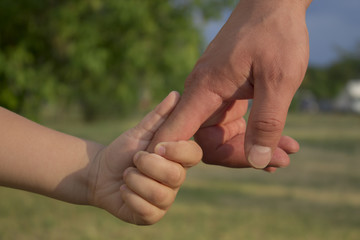 son holds his father's hand, outdoors, close-up