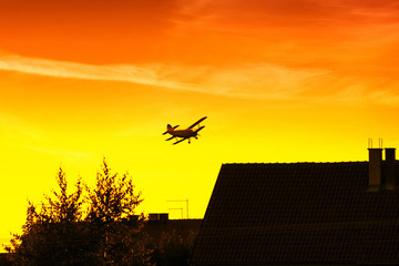 Biplane flying over roofs in vibrant sunset