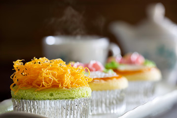 Three Cup cakes decorated topping with Foy Thong (Thai candy made by eggs and syrup) and cream in white plate and English tea