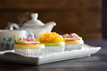 Three,Cup cakes decorated topping with Foy Thong (Thai candy made by eggs and syrup) and cream in white plate and English tea
