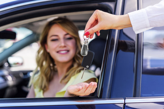 An attractive woman in a car gets the car keys. Rent or purchase of auto.