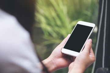 Mockup image of a woman holding white smart phone with blank black desktop screen with blur green nature background