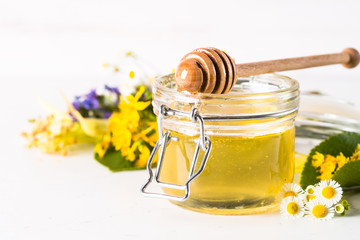 Honey  in a jar with wild herbs on white
