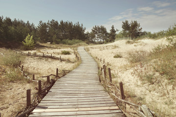 Fototapeta premium Dunes with wooden walkway over sand near Baltic sea. Board way over sand of beach dunes in Lithuania.