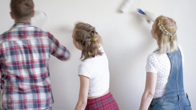 Father, mother and daughter painting wall in apartment room. Beautiful young family doing repairs in new flat. Parents and teen girl making decorate room, laughing and having fun.