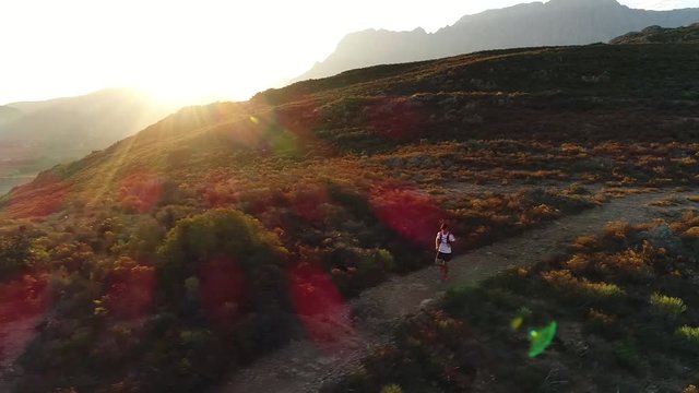 aerial drone footage of a male trail runner running along a single track path through a mountain landscape at sunset