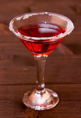 Red cocktail with decorated sugar on a wooden table seen close up
