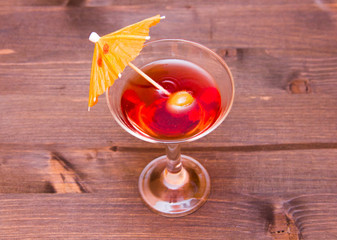 Red cocktail with umbrella on a wooden table seen from above