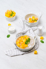 Thai dessert food style : Top view of homemade sago with coconut milk and topping with mango cut into squares and cantaloupe ball in a white bowl  and placed on a marble table with a tablecloth plaid.