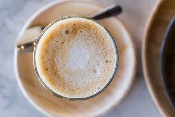Hot latte in a glass cup with spoon and wooden plate. 