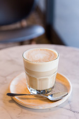 Hot latte in a glass cup with spoon and wooden plate. 