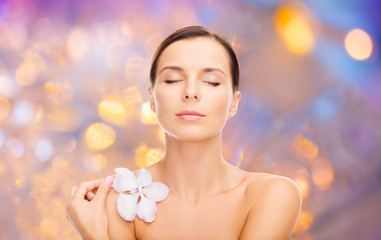wellness and beauty concept - beautiful bare woman with orchid flower over holidays lights background