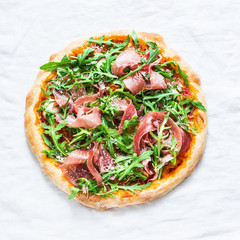 Prosciutto homemade pizza on light background, top view. Delicious appetizers, snack, tapas in mediterranean style. Free space