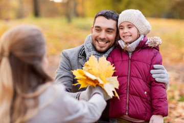 family, season and people concept - happy mother, father and little daughter with maple leaves at autumn park