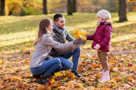 family, season and people concept - happy mother, father and little daughter with maple leaves at autumn park