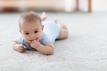 babyhood, childhood and people concept - sweet little asian baby boy lying on floor and sucking...