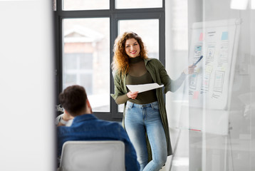 business, technology and people concept - woman showing user interface design on flip chart to creative team at office presentation
