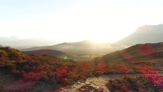 Aerial Drone Tracking Shot Of A Male Trail Runner Running Along A Single Track Path Through A Mountain Landscape At Sunset